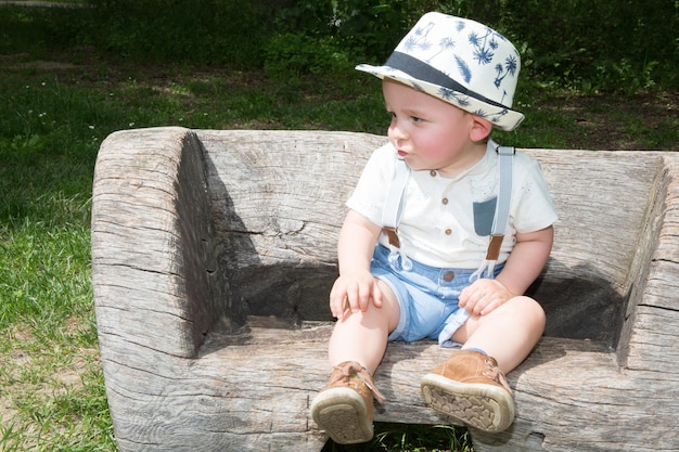 Garçon blond souriant sur un banc dans le parc enfant pensif