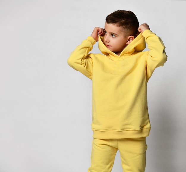 Garçon blond souriant dans un survêtement jaune avec une capuche et un pantalon baskets blanches isolées sur blanc Portrait d'un enfant dans des vêtements cool Vêtements décontractés pour enfants