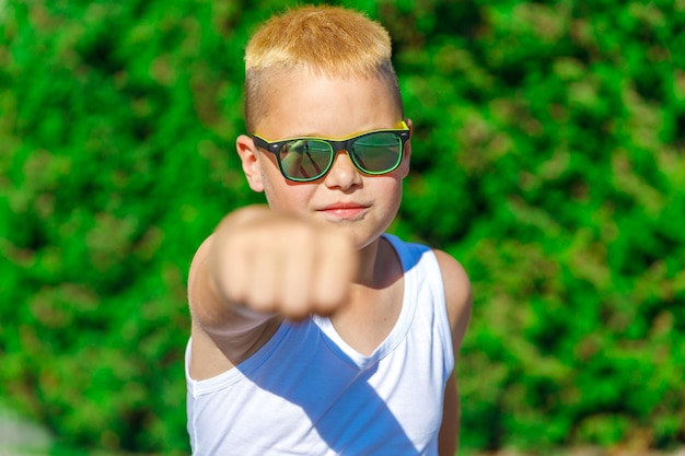 Un garçon blond vêtu d'un t-shirt blanc et de lunettes noires donne un coup de poing en avant