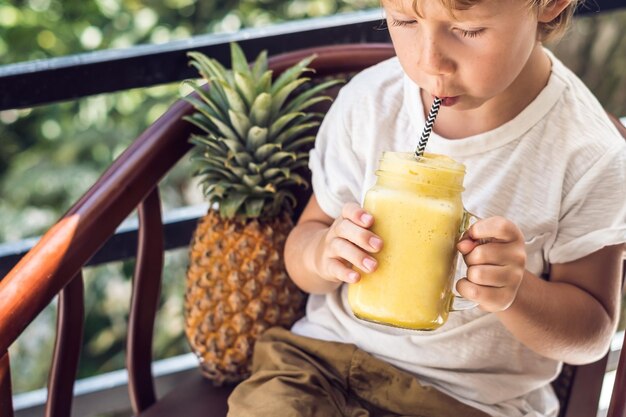 Un garçon boit un smoothie à l'ananas sur la terrasse.