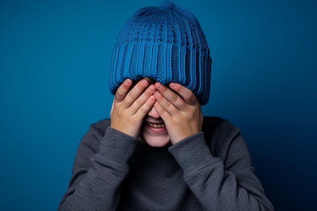 un garçon avec un bonnet tricoté bleu rit sur fond bleu