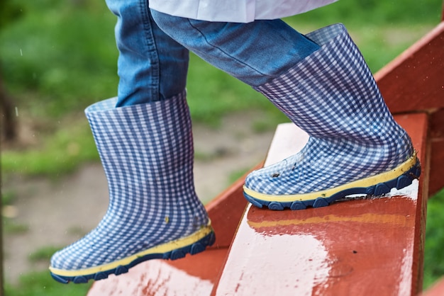 Garçon en bottes de caoutchouc bleu dans les escaliers humides et glissants par jour de pluie. Concept de sécurité des enfants