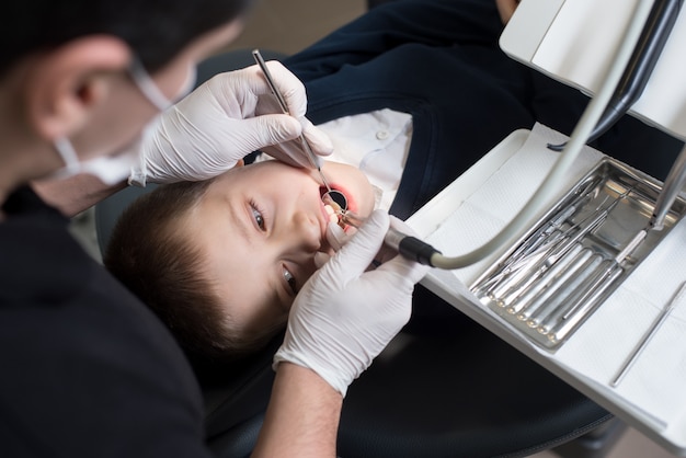 Garçon avec la bouche ouverte pendant le traitement de forage chez le dentiste en clinique dentaire. Fermer. Dentisterie