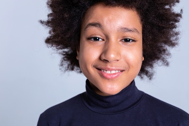 Garçon bouclé se comportant. Joli jeune garçon souriant aux yeux noirs posant pendant une séance photo tout en souriant légèrement