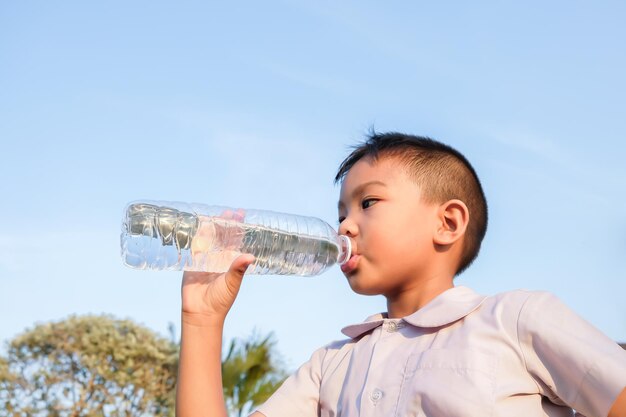 Un garçon buvant de la bouteille d'eau contre le ciel