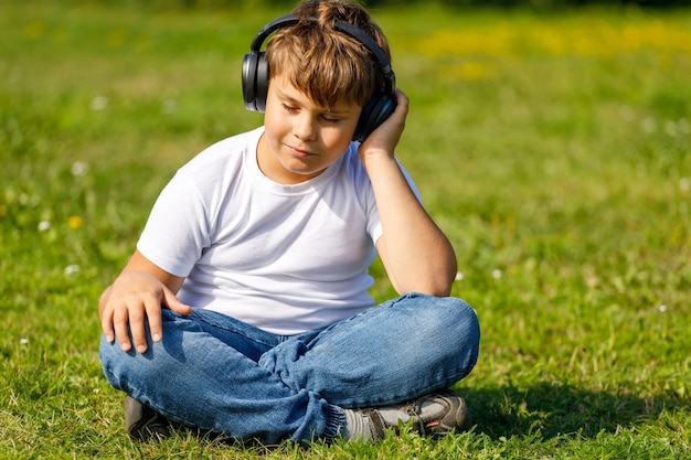 Garçon avec un casque d'écoute de la musique assis sur l'herbe