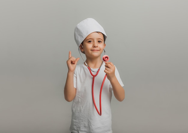 Un garçon à la casquette de médecin tient un stéthoscope sur fond clair. petit docteur. photo de studio de haute qualité