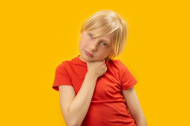 Un garçon caucasien aux cheveux blonds porte un t-shirt rouge et pose pour une photo en studio sur fond jaune