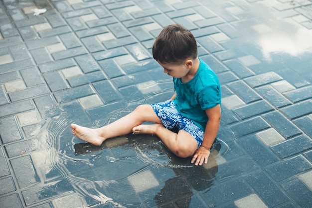 Garçon caucasien jouant avec de l'eau sur le sol dans la cour.