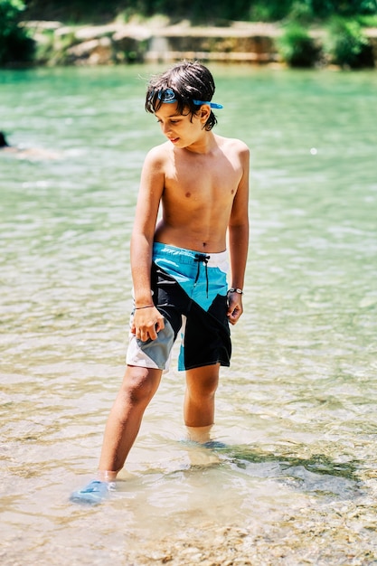 Garçon caucasien en maillot de bain et lunettes de plongée regardant dans l'eau de la rivière en été