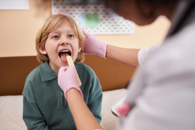 Un garçon caucasien ouvre la bouche pour un examen de la gorge dans une clinique.