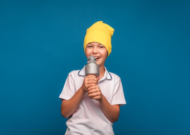 Un garçon chante dans un microphone sur fond bleu Un beau garçon vêtu d'un t-shirt blanc et d'un short se tient sur un fond bleu et chante avec émotion dans le microphone