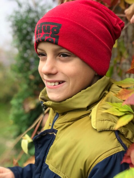 Photo un garçon avec un chapeau rose se tient sur un fond de feuilles d'automne rouges de raisins sauvages et un sourire