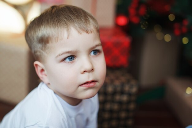 Garçon en chapeaux de Noël est assis avec des coffrets cadeaux dans ses mains avec la joie d'une surprise.