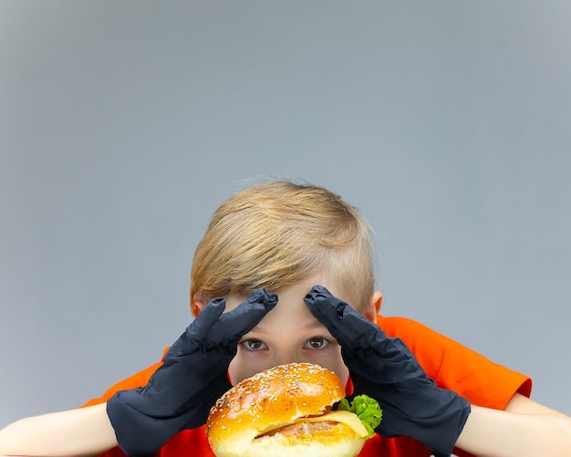 Le garçon avec le cheeseburger se penche sur lui et serre les mains et regarde à travers le hamburger