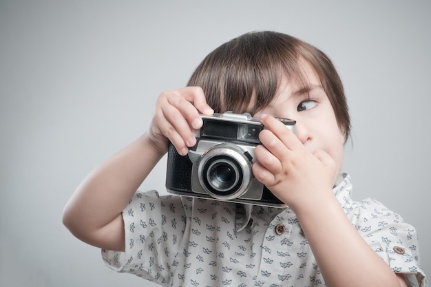 Garçon avec une chemise blanche et des détails bleus prenant des photos avec un appareil photo antique