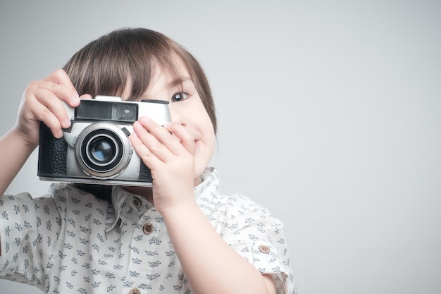 Garçon avec une chemise blanche et des détails bleus prenant des photos avec un appareil photo antique