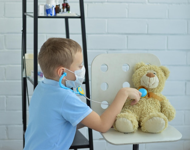 Un garçon en chemise bleue joue au docteur en écoutant le cœur d'un ours en peluche avec un phonendoscope
