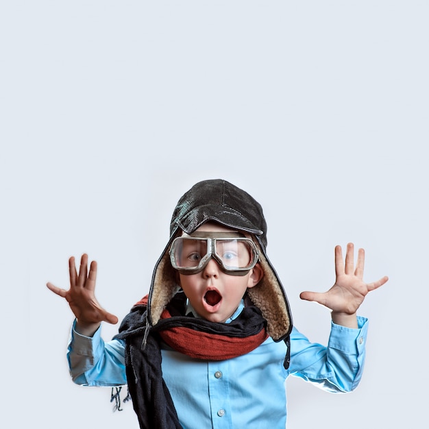 Garçon à la chemise bleue, lunettes de pilote, bonnet et écharpe levant les mains