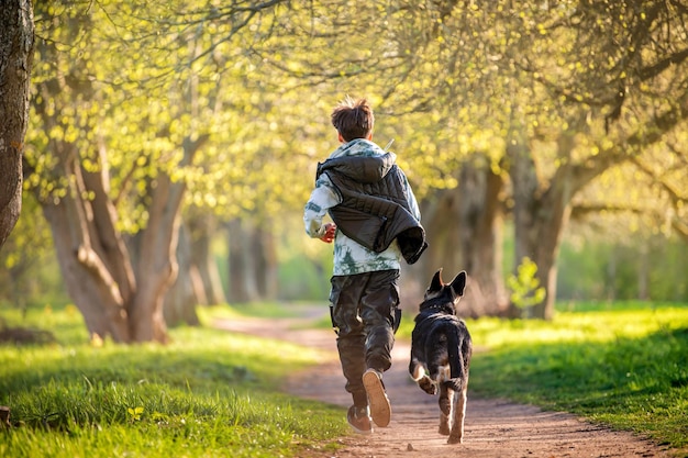 Un garçon avec un chien se promène dans le parc lors d'une soirée de printemps ensoleillée courir le long de la route Amitié de l'homme et de l'animal mode de vie sain