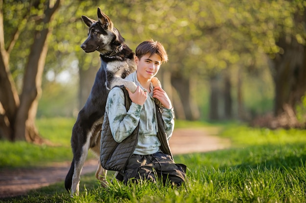 Un garçon avec un chien se promène dans le parc lors d'une soirée de printemps ensoleillée s'asseoir sur l'herbe Amitié de l'homme et de l'animal mode de vie sain