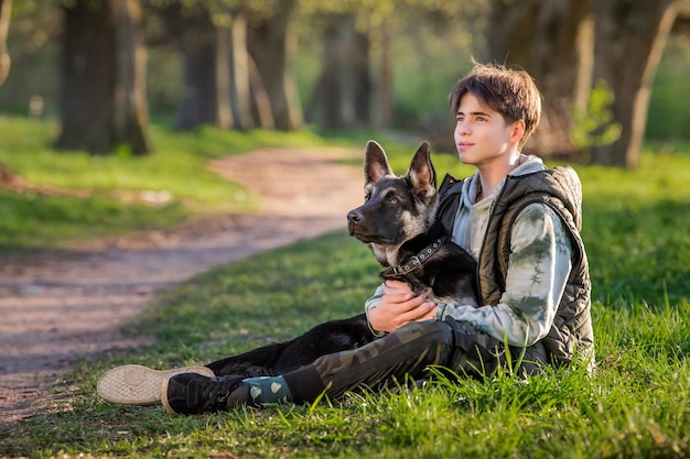 Un garçon avec un chien se promène dans le parc lors d'une soirée de printemps ensoleillée s'asseoir sur l'herbe Amitié de l'homme et de l'animal mode de vie sain