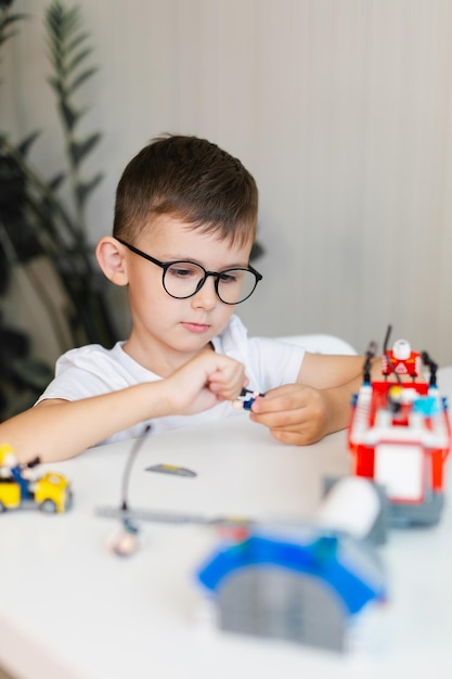 Un garçon de cinq ans avec des lunettes joue avec des briques de construction de jouets colorés