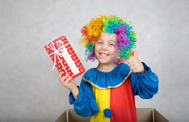 Garçon de cinq ans vêtu du costume d'un clown avec un cadeau. Fermer