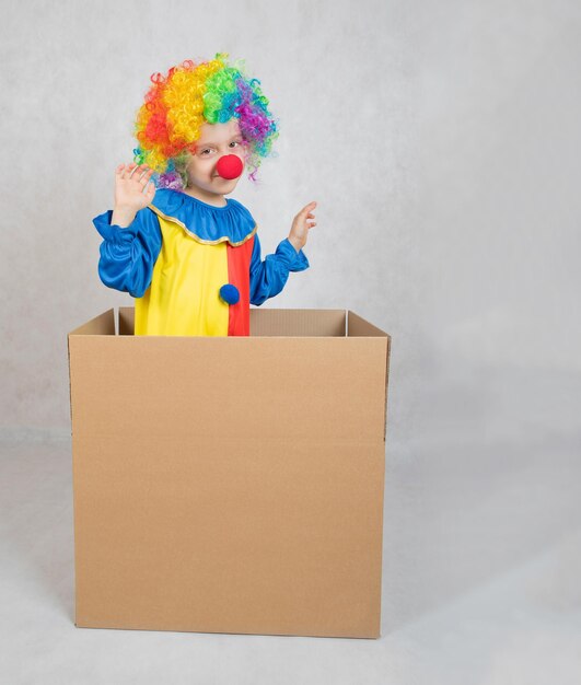 Un garçon de cinq ans vêtu du costume d'un clown reste dans une boîte en carton. Fermer