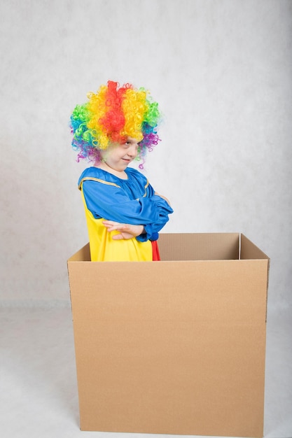 Un garçon de cinq ans vêtu du costume d'un clown reste dans une boîte en carton. Fermer