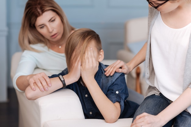 Garçon en colère portant un costume de jeans ayant une coupe de cheveux élégante tenant les mains sur son visage