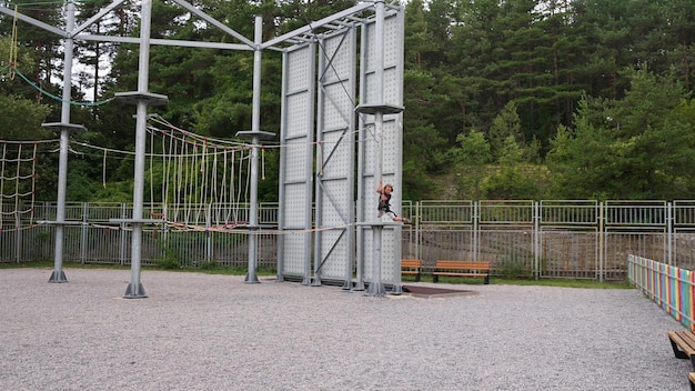 Un garçon courageux dévale en toute confiance des tyroliennes dans un parc accrobranche, ressentant la montée d'adrénaline et conquérant des hauteurs dans une aventure estivale en toute sécurité.