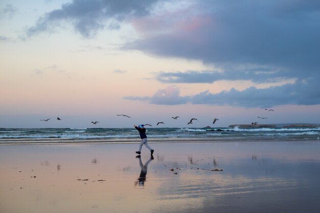 Garçon en cours d'exécution avec des oiseaux sur la plage d'hiver près de l'océan