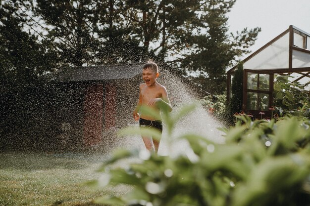 Un garçon court sur l'herbe sous le jet d'eau de l'arroseur