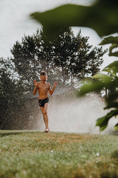 Un garçon court sur l'herbe sous le jet d'eau de l'arroseur