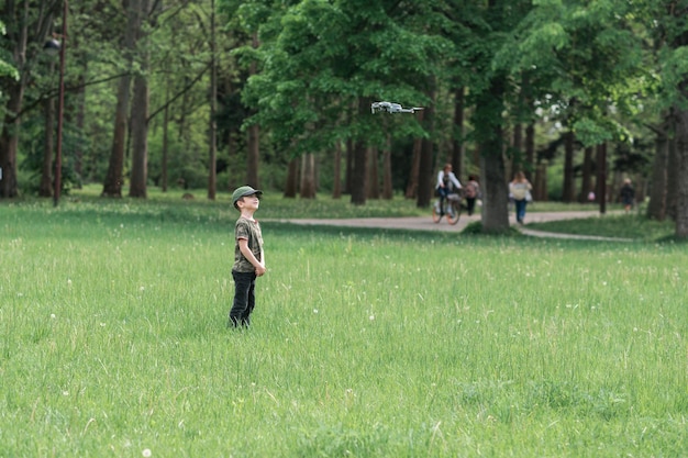 Le garçon court sur l'herbe verte du parc et un drone le survole Garçon jouant avec un drone