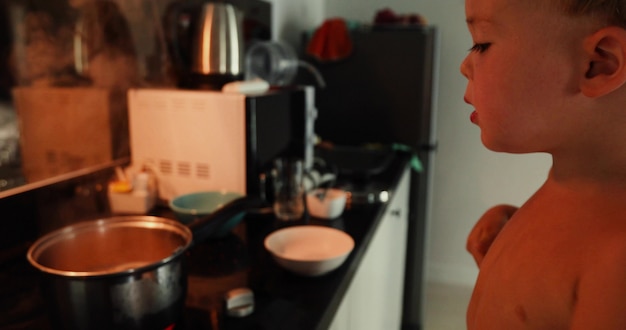 Garçon cuisine par elle-même à la maison. Un enfant sort une fourchette chaude et se brûle