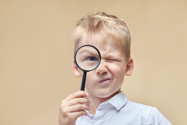 Un garçon curieux regarde à l'avant à travers une loupe et fait une grimace.