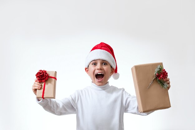 Le garçon dans un bonnet rouge crie tout en tenant des cadeaux de Noël. Concept de Noël.