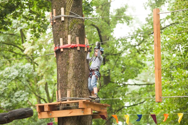 Un garçon dans un casque et un équipement de sécurité dans un parc de cordes d'aventure sur fond de nature