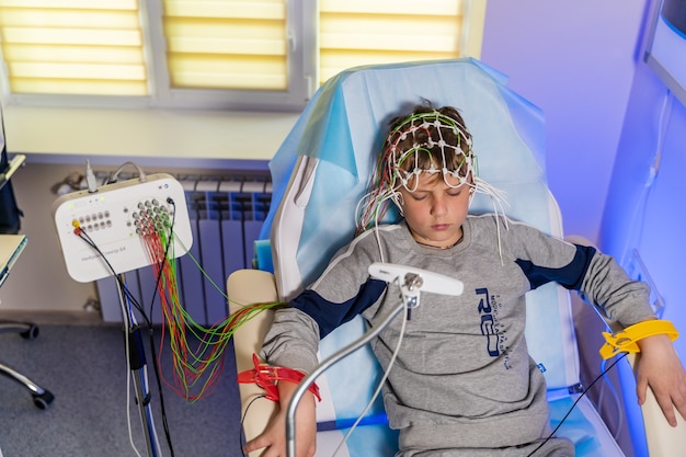 Garçon dans une casquette spéciale pendant l'électroencéphalographie à côté du moniteur avec des lectures.