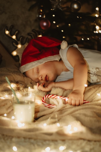 un garçon dans un chapeau du Nouvel An. un bébé dans un bonnet de Noel dort sous le sapin de Noël