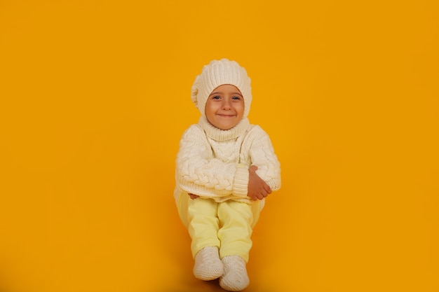 un garçon dans un chapeau d'hiver blanc dans un pull blanc tricoté et des chaussettes sur fond jauneblanc