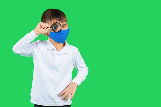 Un garçon dans une chemise blanche et un masque de protection regarde à travers une loupe dans la distance