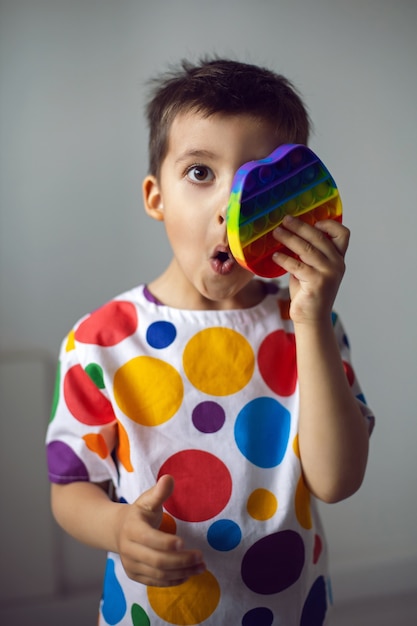 Garçon dans une chemise avec des cercles colorés joue avec un jouet pop it en silicone