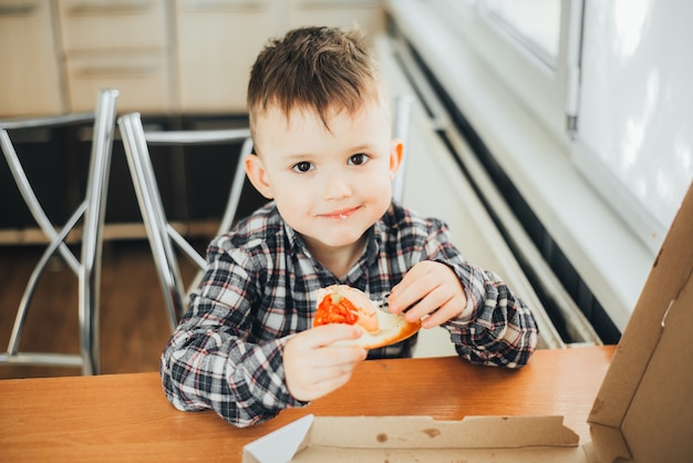 Le garçon dans la cuisine à la maison manger de la pizza au saumon