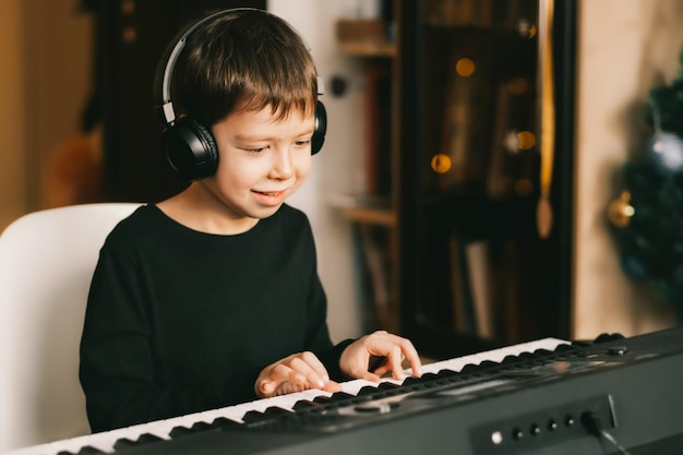 Un garçon dans des écouteurs sans fil joue du piano sur fond de guirlande de Noël