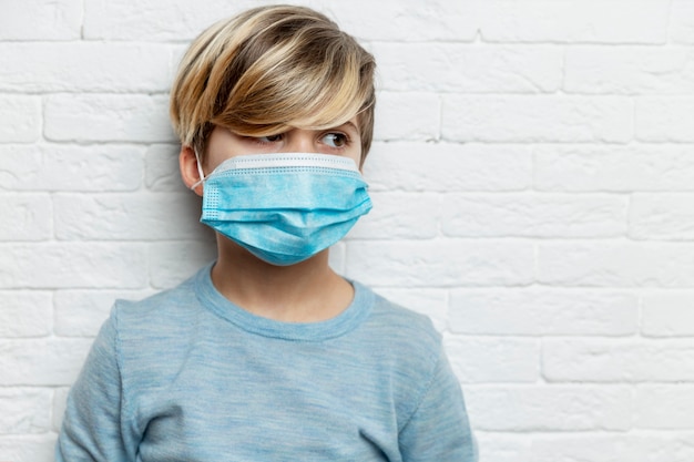 Garçon dans un masque médical. Un garçon de 9 ans dans un pull bleu regarde sur le côté.