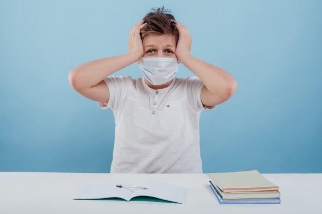 Garçon dans le masque médical a mal à la tête avec ses mains sur sa tête isolé sur fond blanc assis...