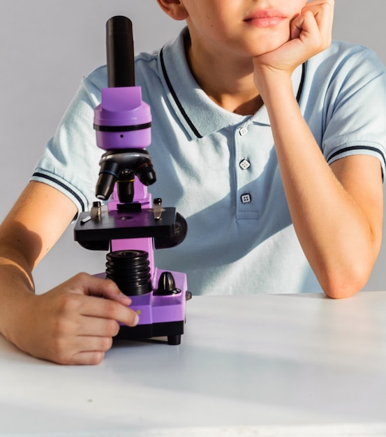 Un garçon dans un polo bleu regarde tenant un microscope violet dans ses mains regarde par la fenêtre et rêve